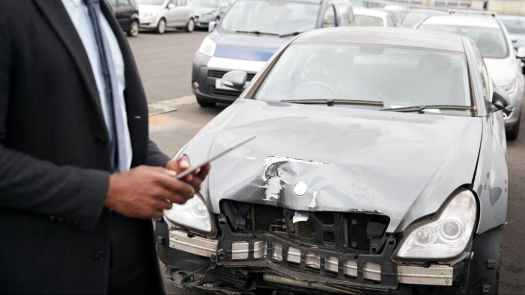 Insurance adjuster with a tablet reviewing front-end damage on a black car.