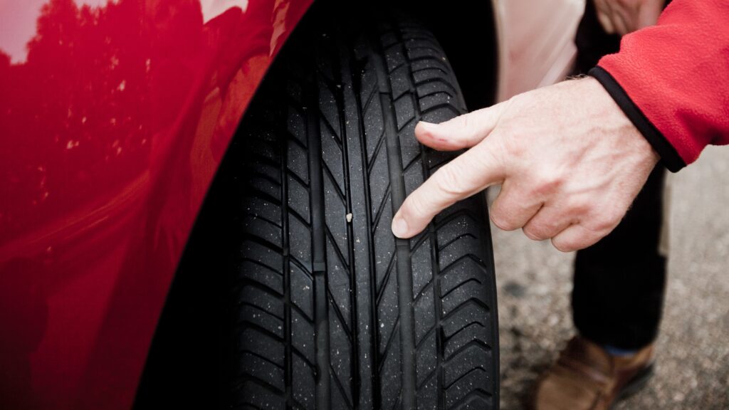 Driver inspecting a tire for wear or damage, a common maintenance habit to help prevent accidents on Texas roads.