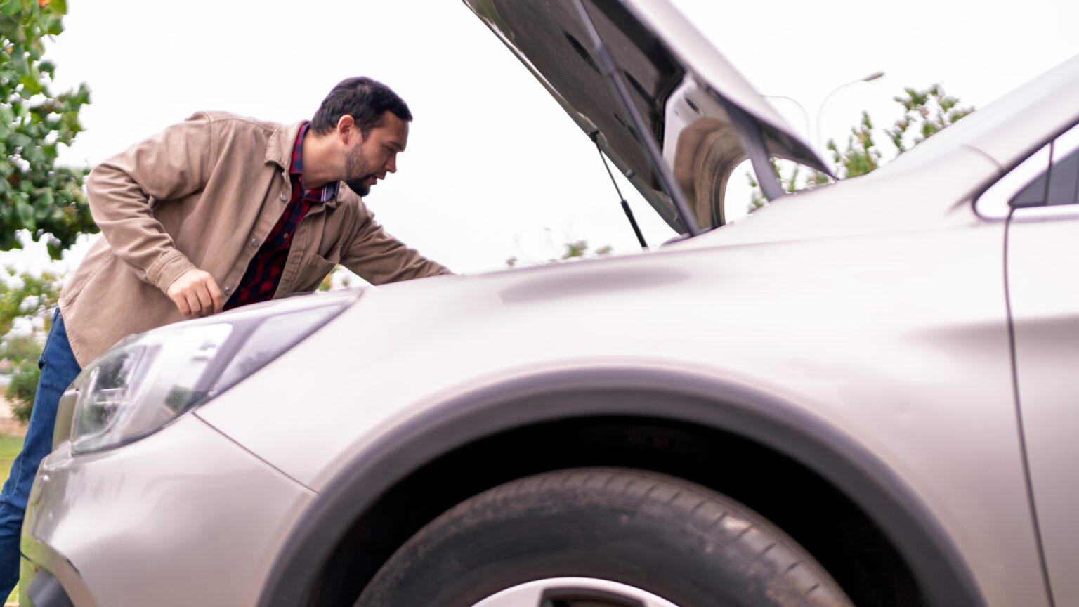 Man checking under the hood of his car to prevent accidents and avoid mechanical failures before driving long distances.