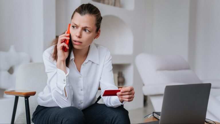 Concerned woman holding a phone and credit card while talking during a suspicious call from a possible fake injuty lawyers calls