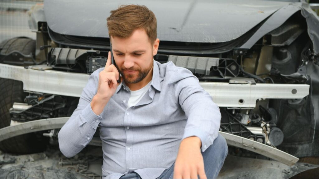 Man sitting near a damaged car and calling for help after a car accident during the holiday in Florida.