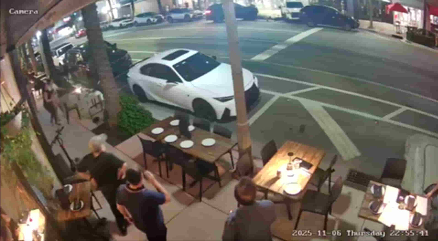 Surveillance image showing bystanders reacting after the Surfside car accident in Miami near a busy restaurant sidewalk.